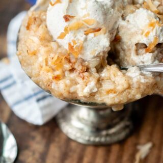 a serving bowl of rice pudding with toasted coconut and whipped cream on top.
