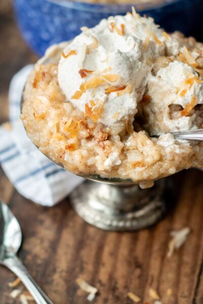 a serving bowl of rice pudding with toasted coconut and whipped cream on top.