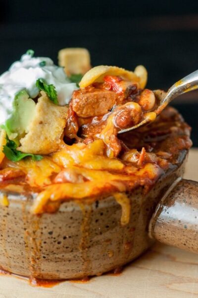 a close up of a spoon taking out a bite of chicken chorizo chili with cheese
