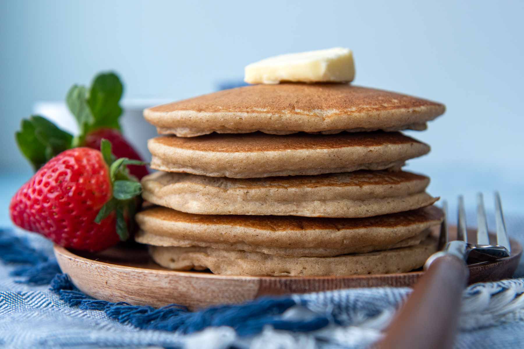 a stack of flourless pancakes on a wood plate with a piece of butter on top