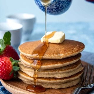 syrup being poured on uncut flourless pancakes stack