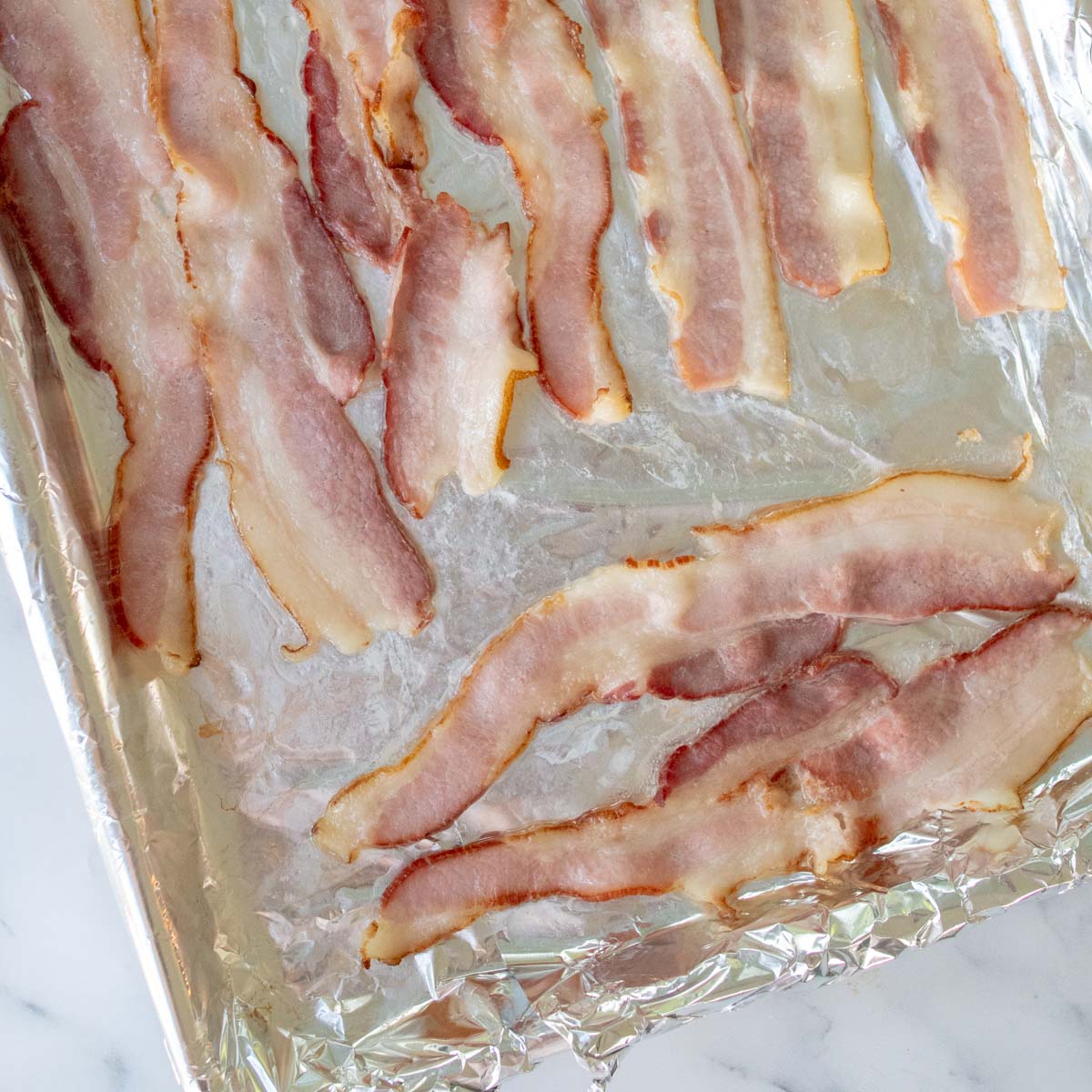 partially cooked bacon on a foil lined sheet