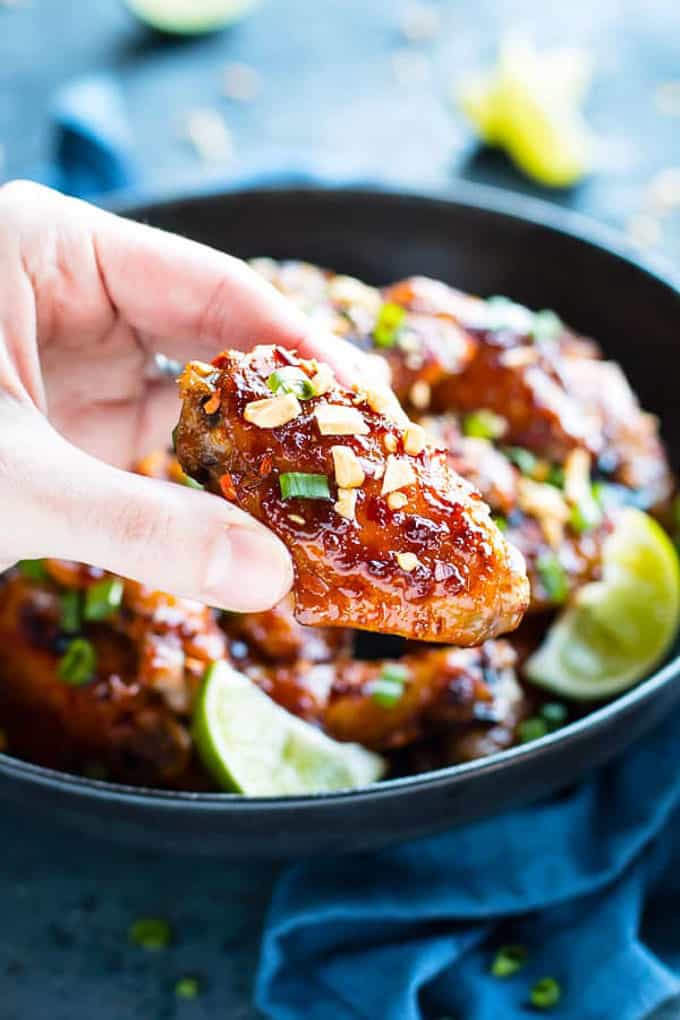 a hand holding up a sticky asian chicken wing for watching the big game