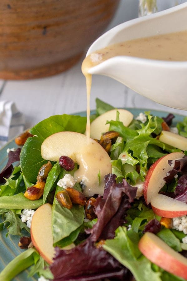 maple vinaigrette being poured from a white dressing container onto the apple pecan salad