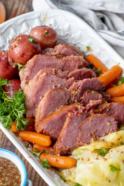 sliced corned beef with cabbage, potatoes, and carrots on a white platter