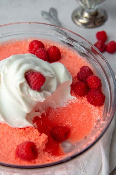 a bowl of jello with raspberries and cool whip on top and a scoop taken out