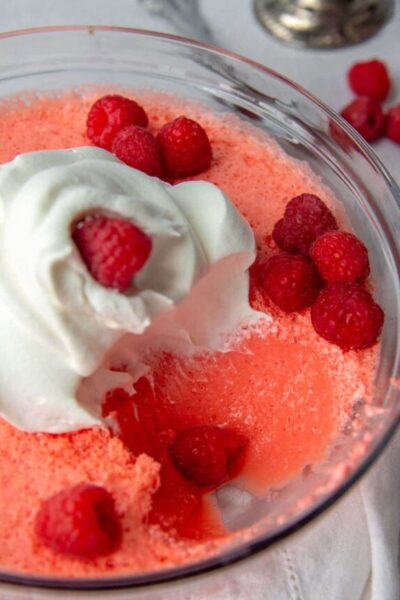 a bowl of jello with raspberries and cool whip on top and a scoop taken out