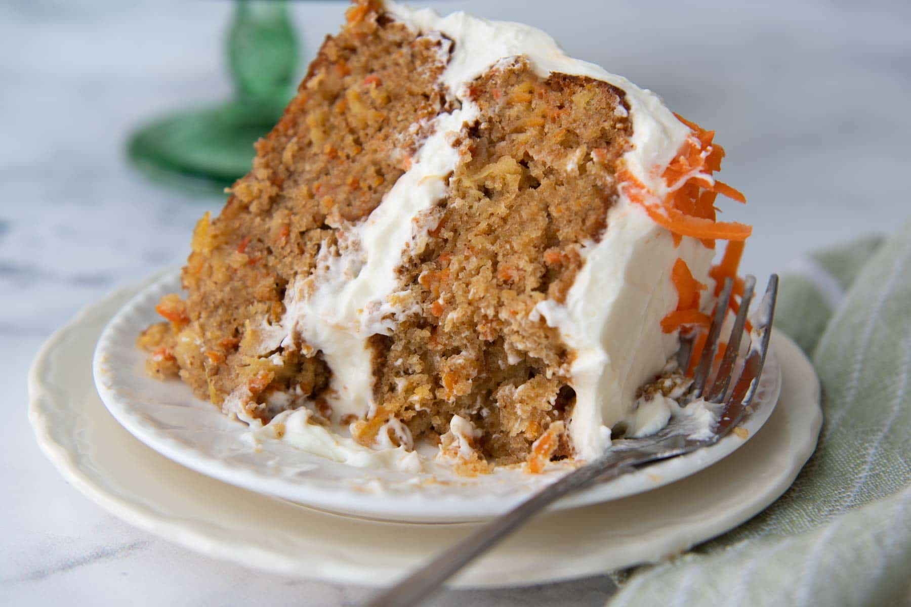a slice of carrot cake on a white plate with a bite taken out
