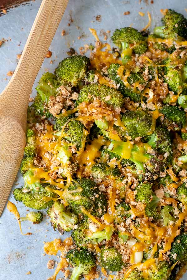 an overhead shot of baked broccoli and cheese in a pile on a baking sheet with a wooden server laying next to it