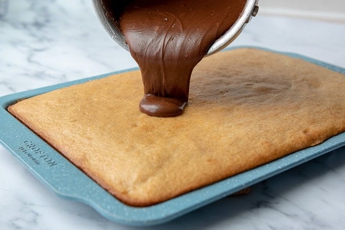 chocolate frosting being poured onto peanut butter cake