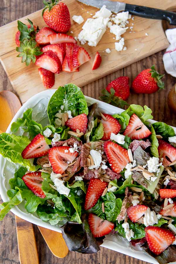 an overhead shot of strawberry salad in a white bowl with cutting board next to it