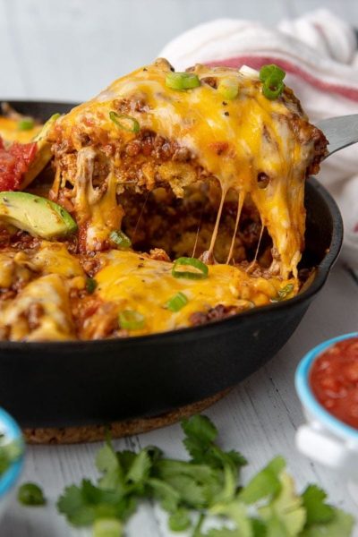 a slice of tamale pie being lifted out of a cast iron skillet with cheese stringing off