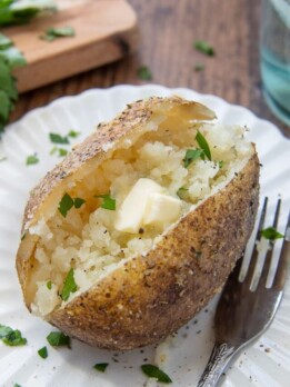an instant pot baked potato on a white plate with a fork nearby with melting butter in the middle