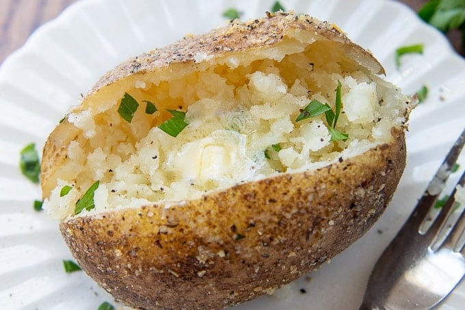 a close up of crispy skinned baked potato with melting butter and parsley garnish