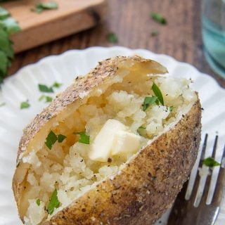an instant pot baked potato on a white plate with a fork nearby with melting butter in the middle