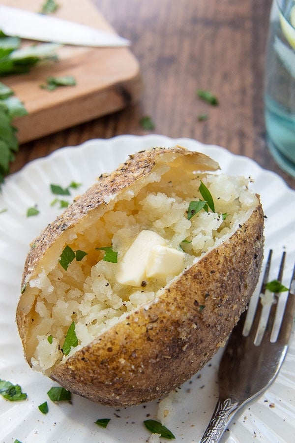 an instant pot baked potato on a white plate with a fork nearby with melting butter in the middle