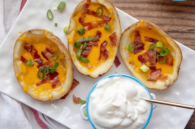 3 potato skins on a white rectangular plate with a small dish of sour cream in the middle