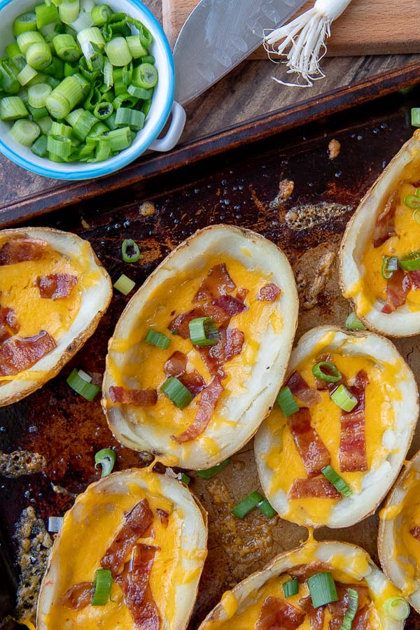 a close up overhead shot of potato skins on a baking sheet with cut green onions sprinkled around