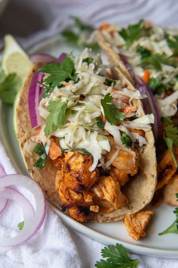 a close up of buffalo chicken tacos with a blue cheese slaw on top with sliced red onions on plate