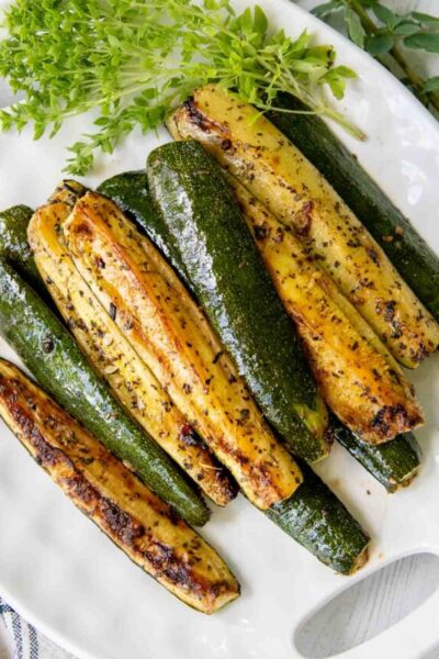 roasted zucchini on a white plate with fresh herbs next to it.
