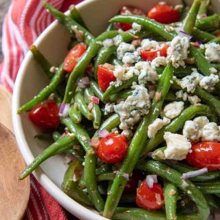 a close up of a serving bowl of beans, blue cheese and tomatoes