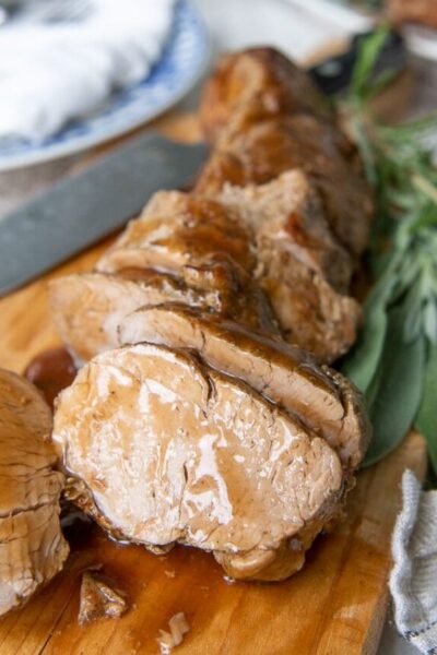 cut pieces of pork tenderloin on a wooden cutting board with sauce drizzled over