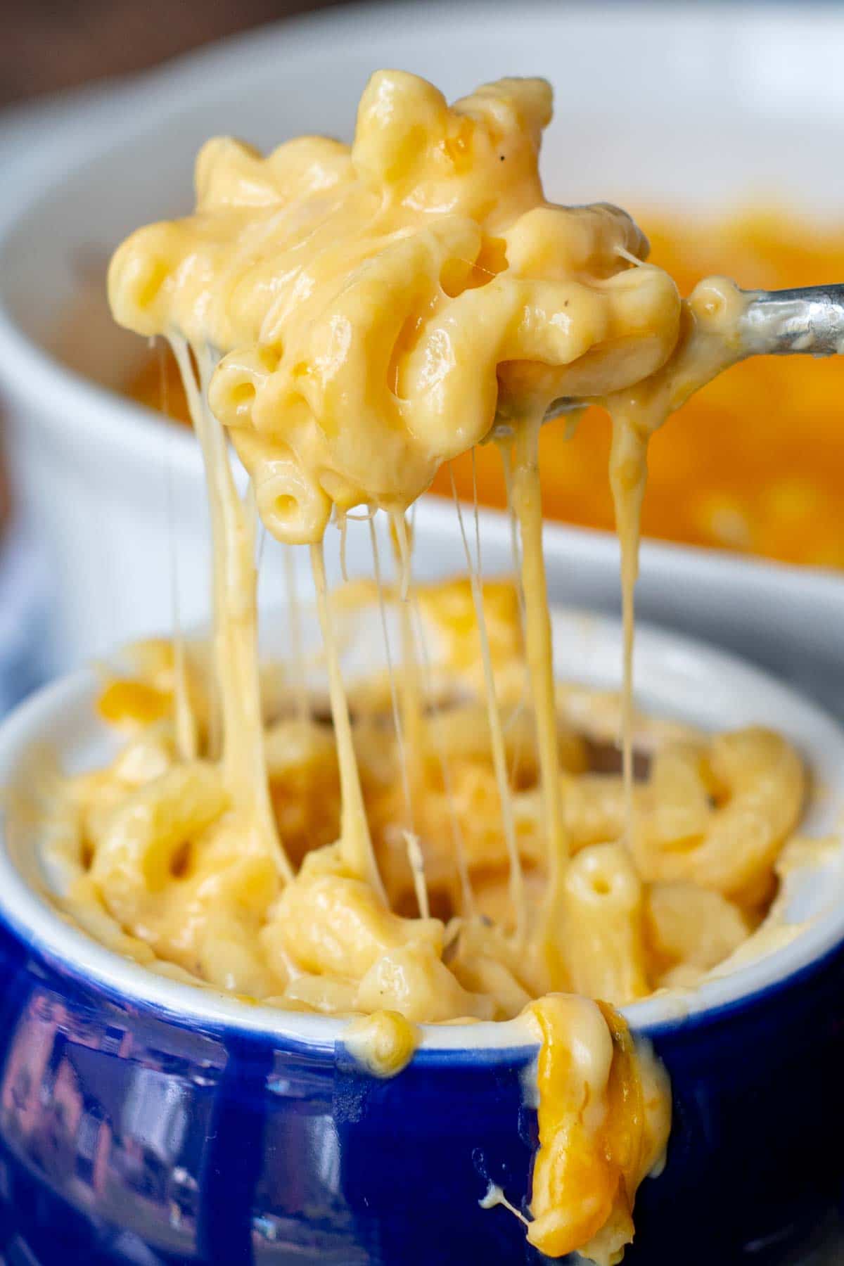 a spoon lifting out a bite of mac and cheese from a blue bowl