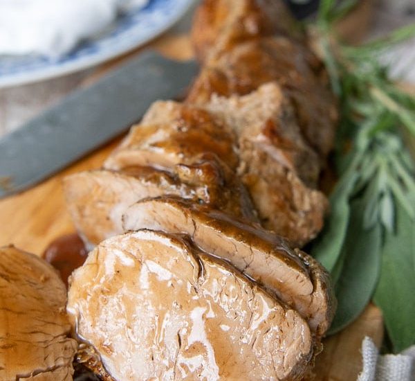 cut pieces of pork tenderloin on a wooden cutting board with sauce drizzled over