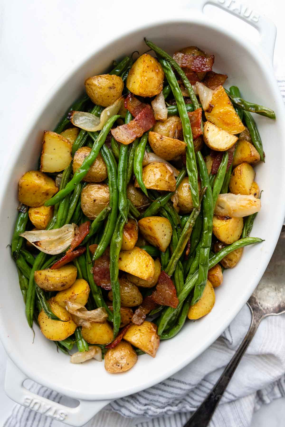 a serving dish full of green beans, potatoes, and bacon with onion.