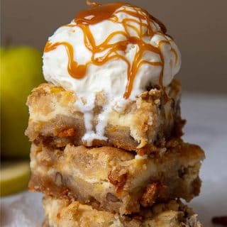 a tower of caramel apple cheesecake bars with a scoop of ice cream melting down and caramel sauce