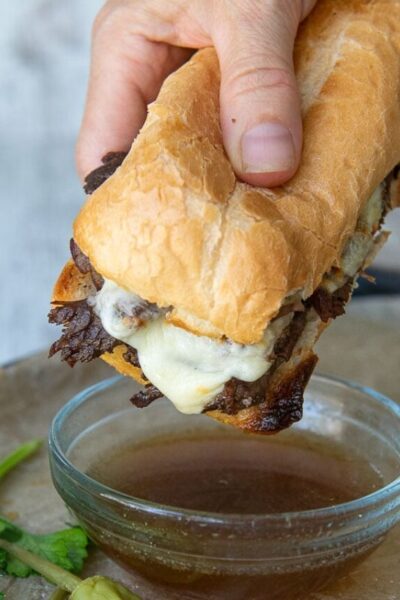 a hand holding french dip sandwich about to be dipped into au jus