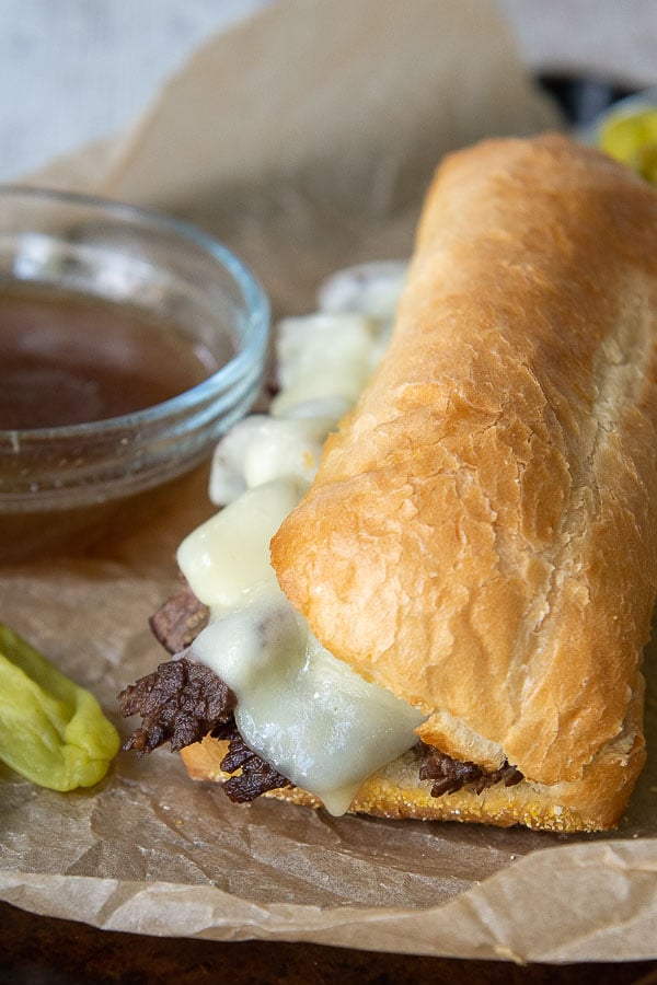 a french dip sandwich laying on a baking sheet with a cup of beef broth to dip in next to it