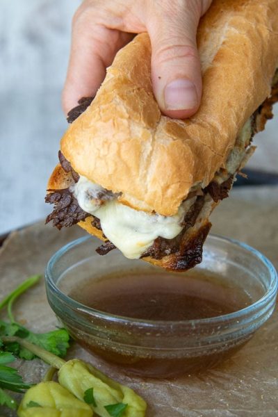 a hand holding french dip sandwich about to be dipped into au jus