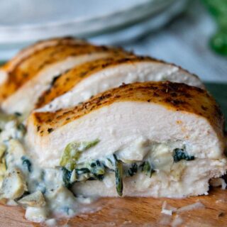 close up of sliced spinach artichoke chicken on a wooden cutting board.