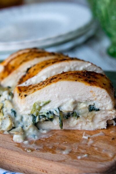 close up of sliced spinach artichoke chicken on a wooden cutting board.