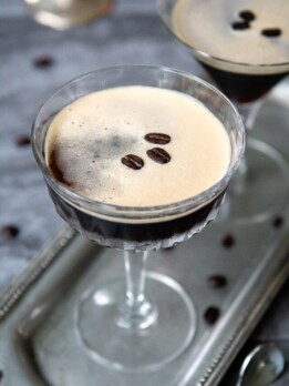 2 espresso martinis on silver tray with espresso beans all around