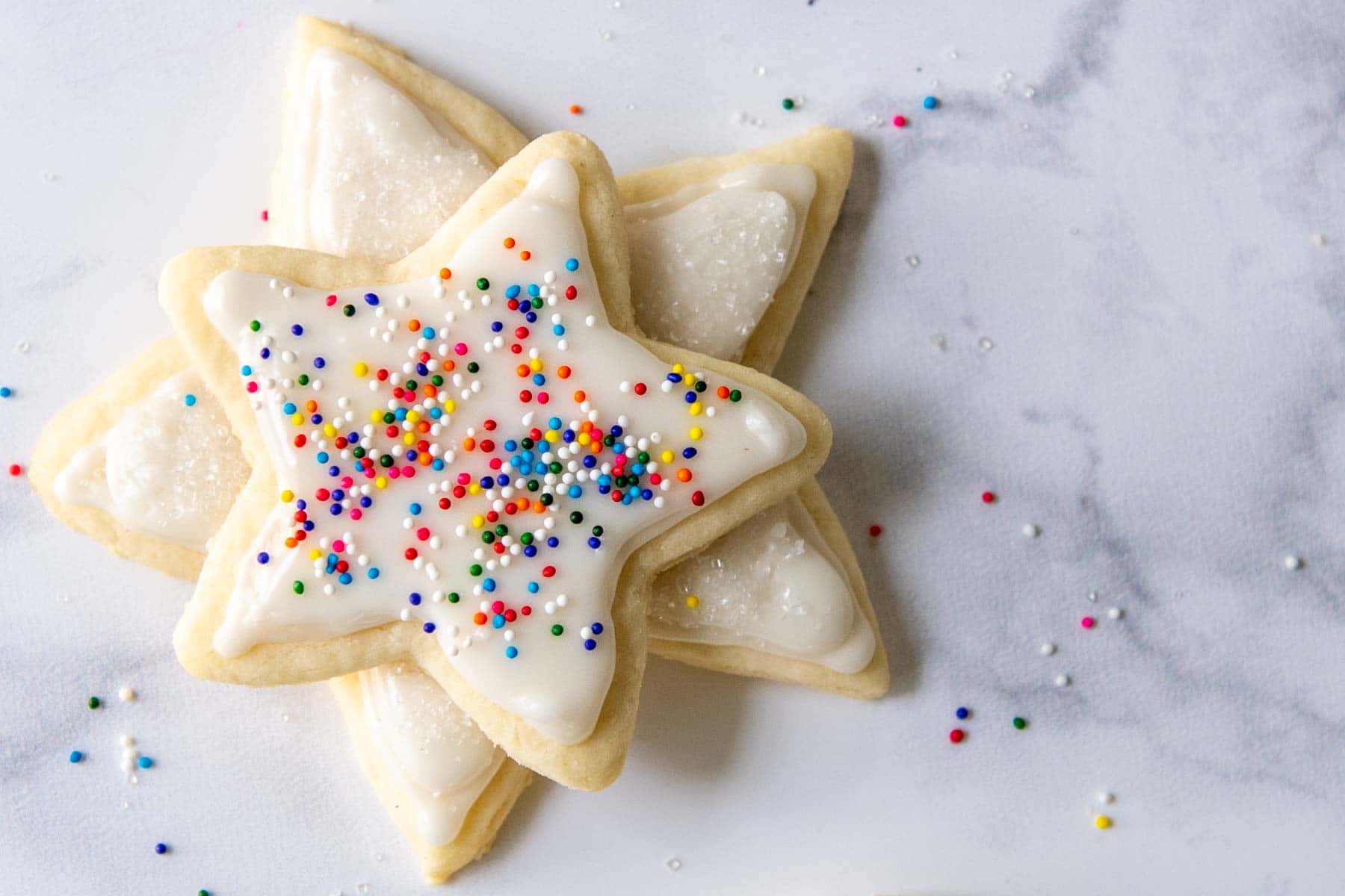 two gluten-free sugar cookies cut out in star shapes with white frosting and sprinkles