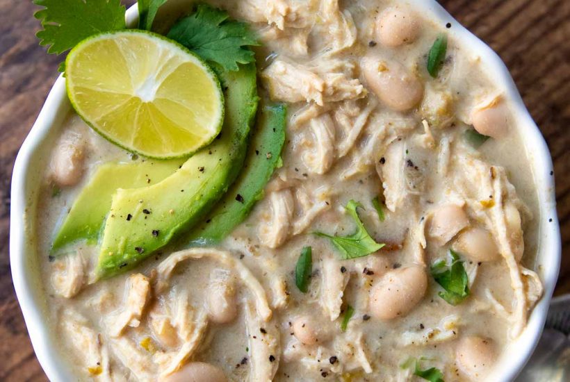 overhead shot of instant pot white chicken chili with sliced avocados, cilantro, and lime wedge on top