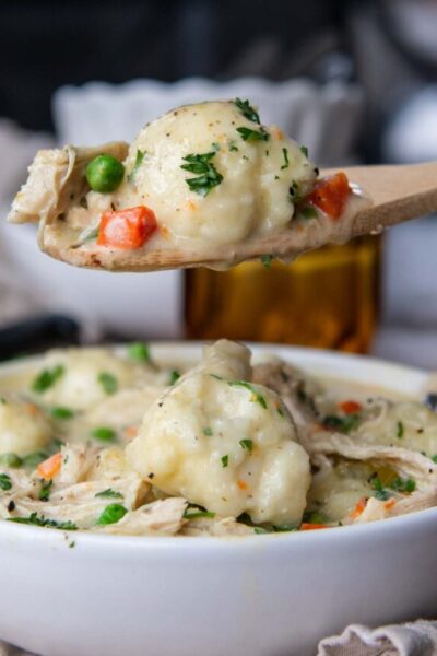 a wooden spoon holding up a scoop of chicken and dumplings
