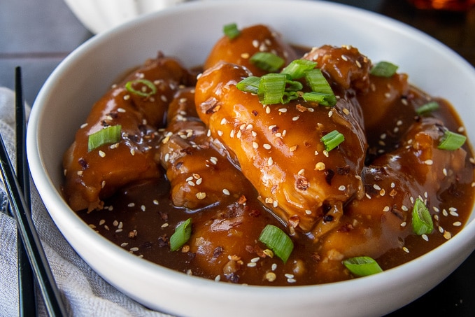 honey soy chicken thighs with sauce in a white bowl with chopsticks laying next to it