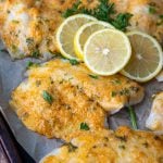 parmesan crusted tilapia on a baking sheet with lemon slices on top