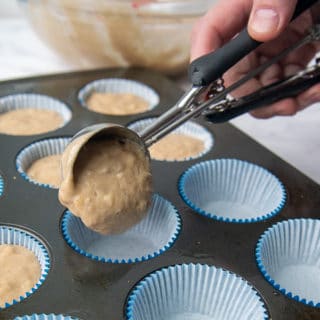 muffin batter being placed in a muffin tin with an ice cream scoop