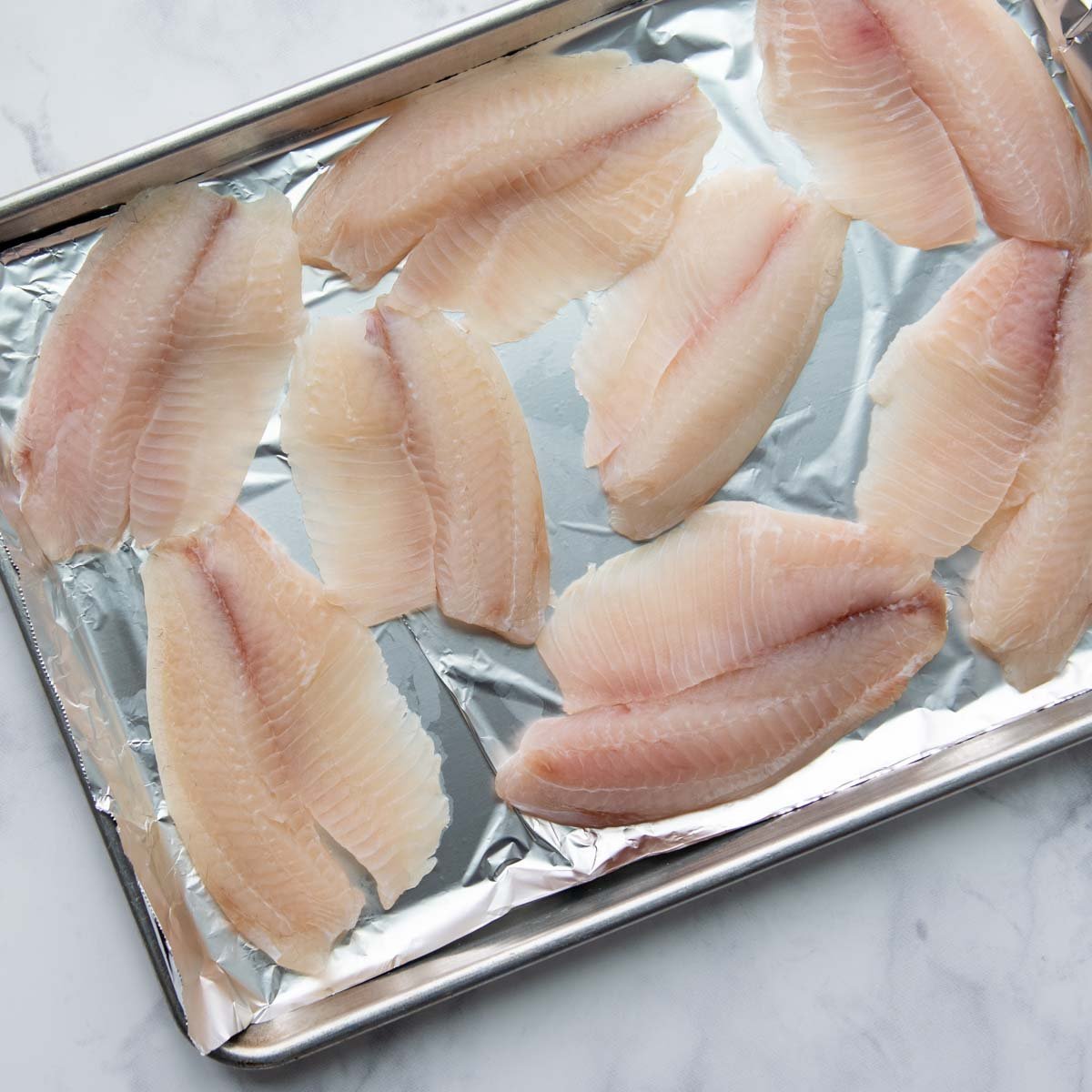 unbaked tilapia on a foil lined baking sheet
