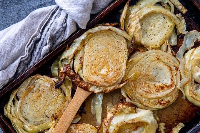a wooden spatula holding up a roasted cabbage slice from a sheet pan