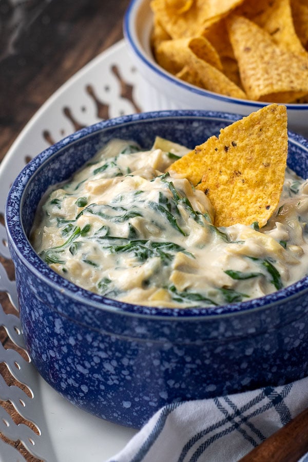 a chip resting in a bowl of spinach artichoke dip sitting on a serving tray
