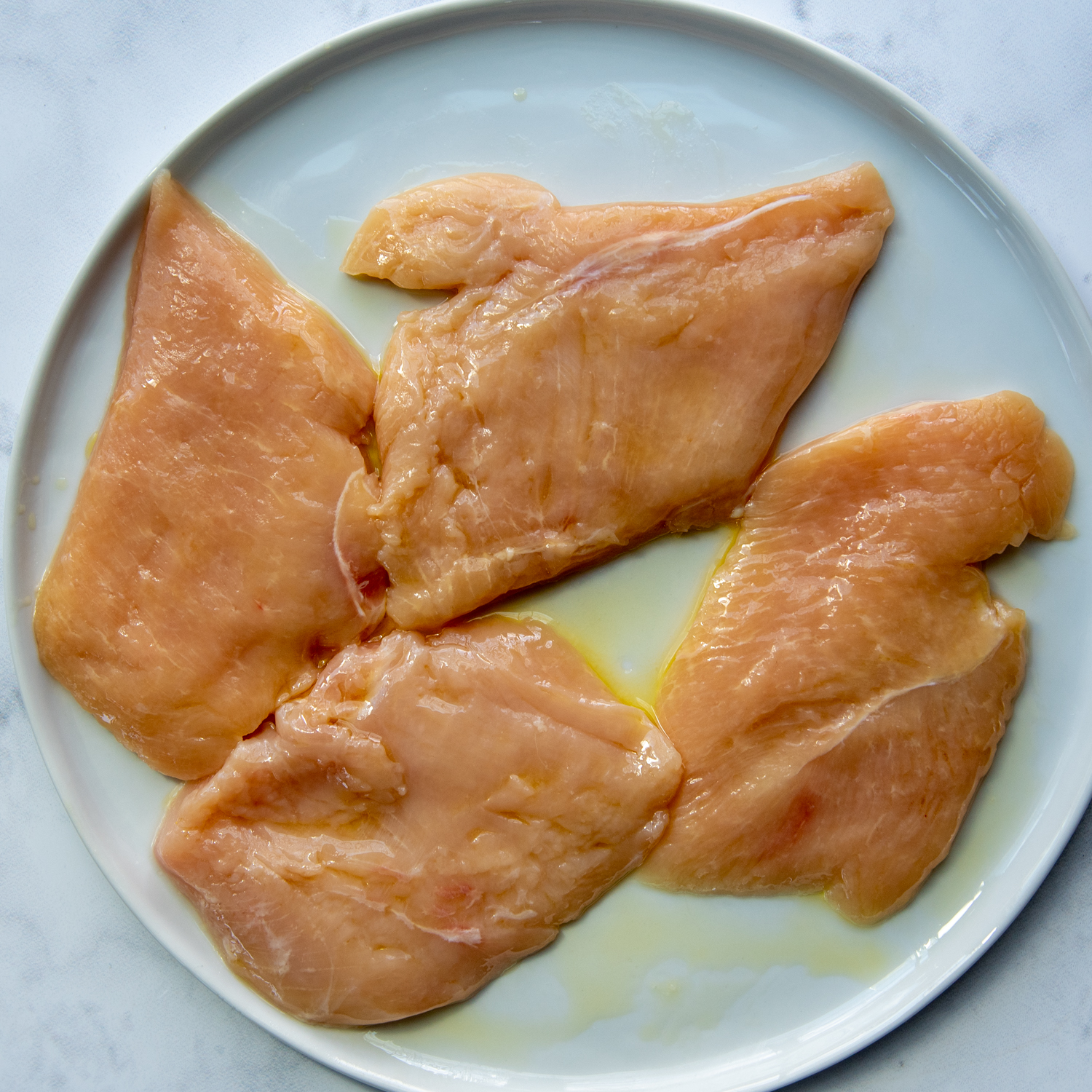 chicken cutlets on a plate with oil drizzled on.