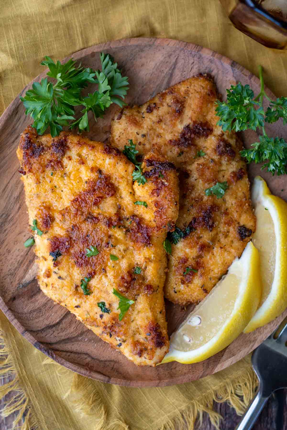 bread chicken cutlets on a wood plate with parsley and lemon