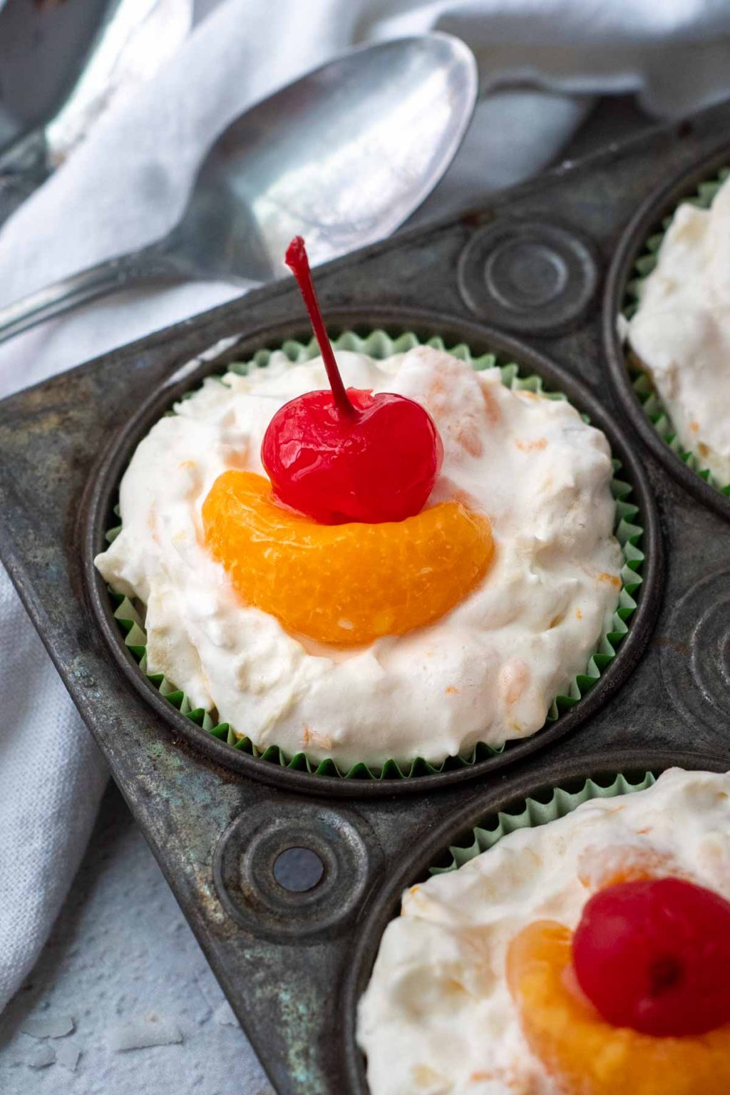 top view of fruit salad cups in a muffin tin with orange and cherry on top