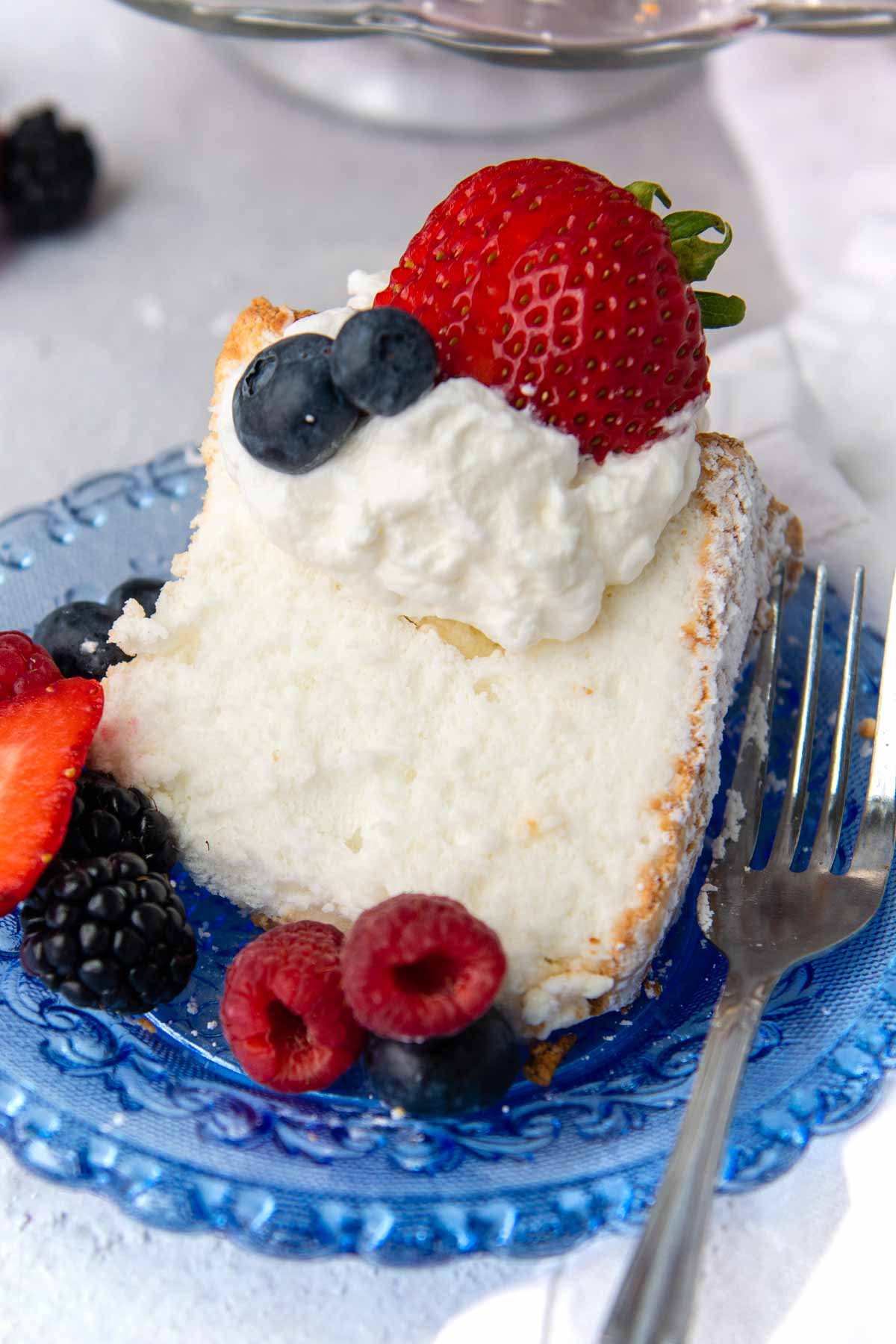 a slice of angel food cake on a blue plate with whipped cream and fresh fruit on top.