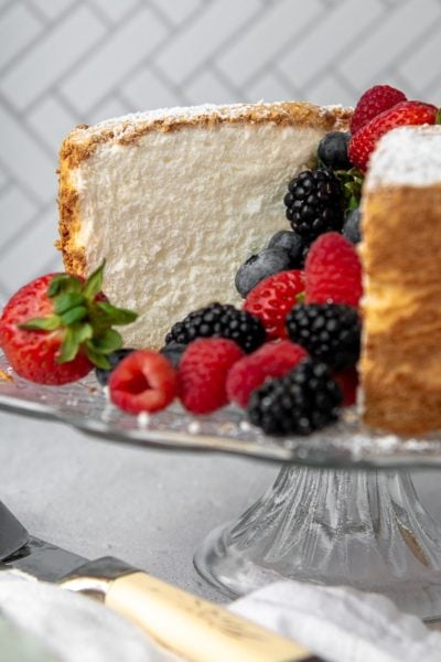 a gluten free angel food cake on a cake stand cut open with berries spilling out